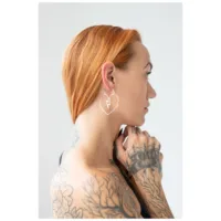 Punatukkainen nainen käyttää rosékultaisia sydänkorvakoruja valkoista taustaa vasten