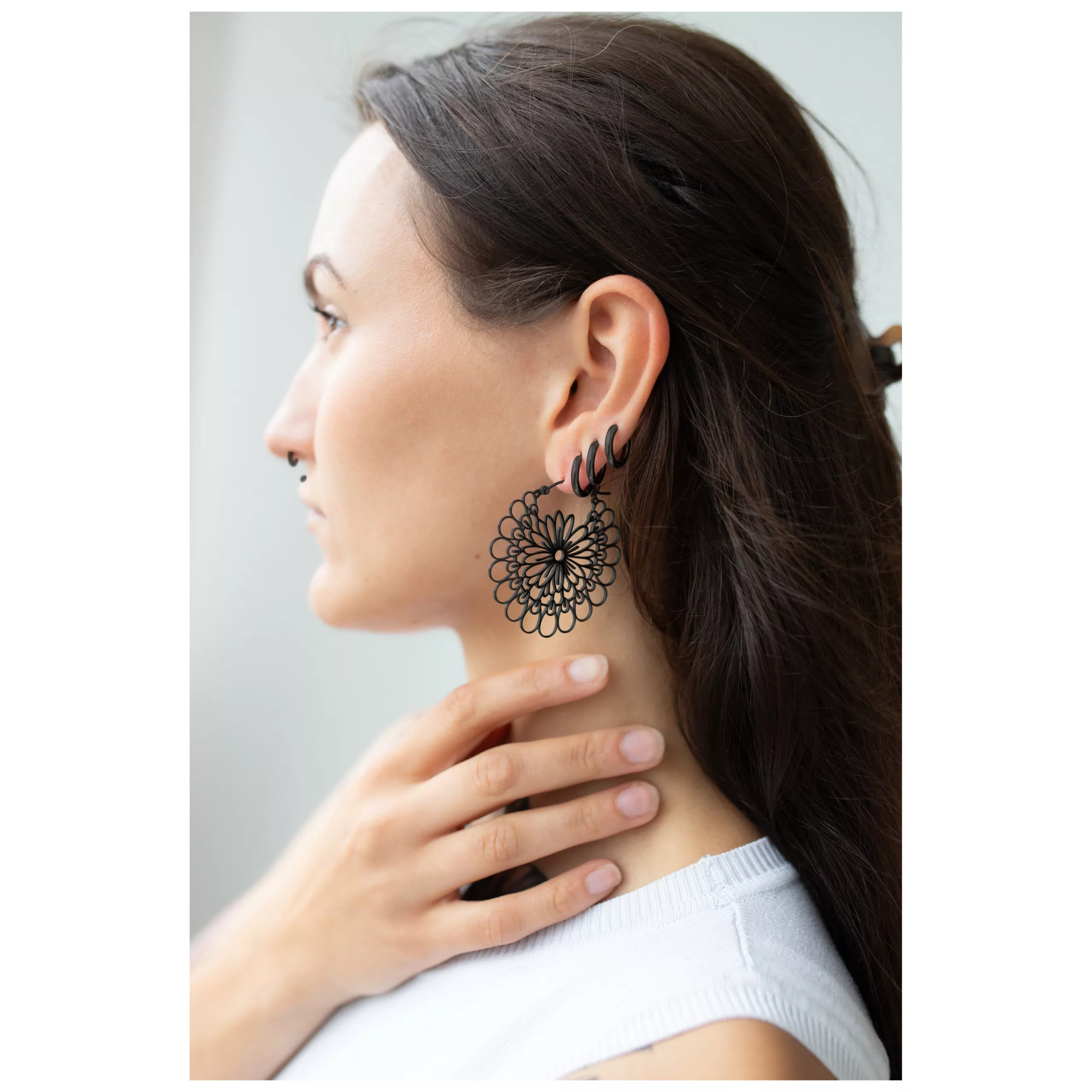 Musta Daisy Hoops -korvakorut kirurginteräksestä Musta Daisy Hoops -korvakorut kirurginteräksestä ruskeahiuksisella naisella, jolla on valkoinen paita