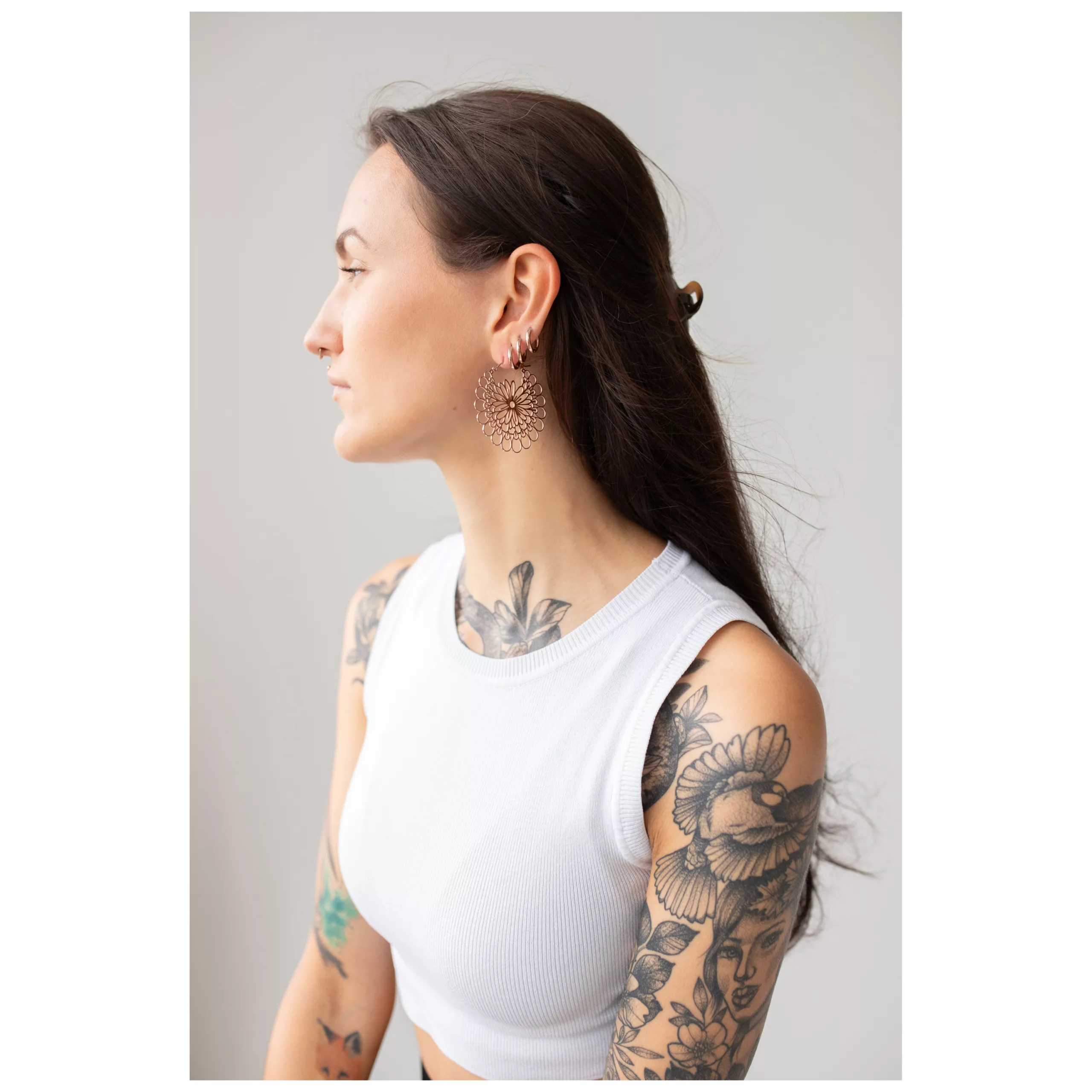 Nainen Daisy Hoops -korvakoruissa ruusukultaa ja tatuointeja, sivulta