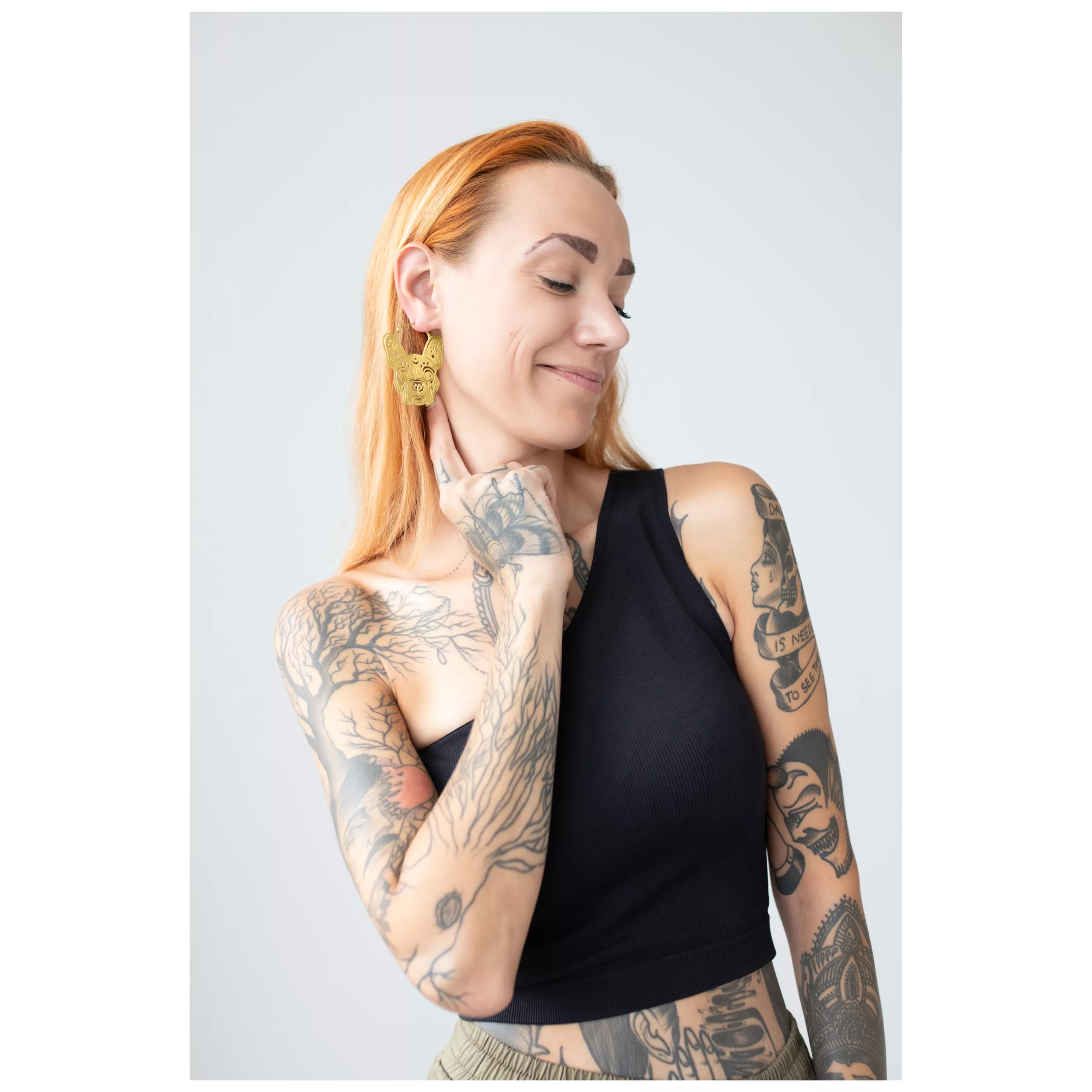 Nainen käyttää kultaisia Bulldog Hoops -korvakoruja, hymyilee tatuointien kanssa