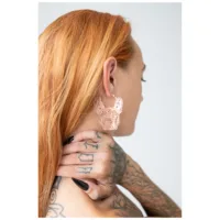 Ruusukultaiset Bulldog-korvakorut henkilön korvassa, jolla on punaiset hiukset ja tatuointeja