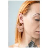 Nainen ruusukultaisilla Bulldog-korvakoruilla vaalealla taustalla