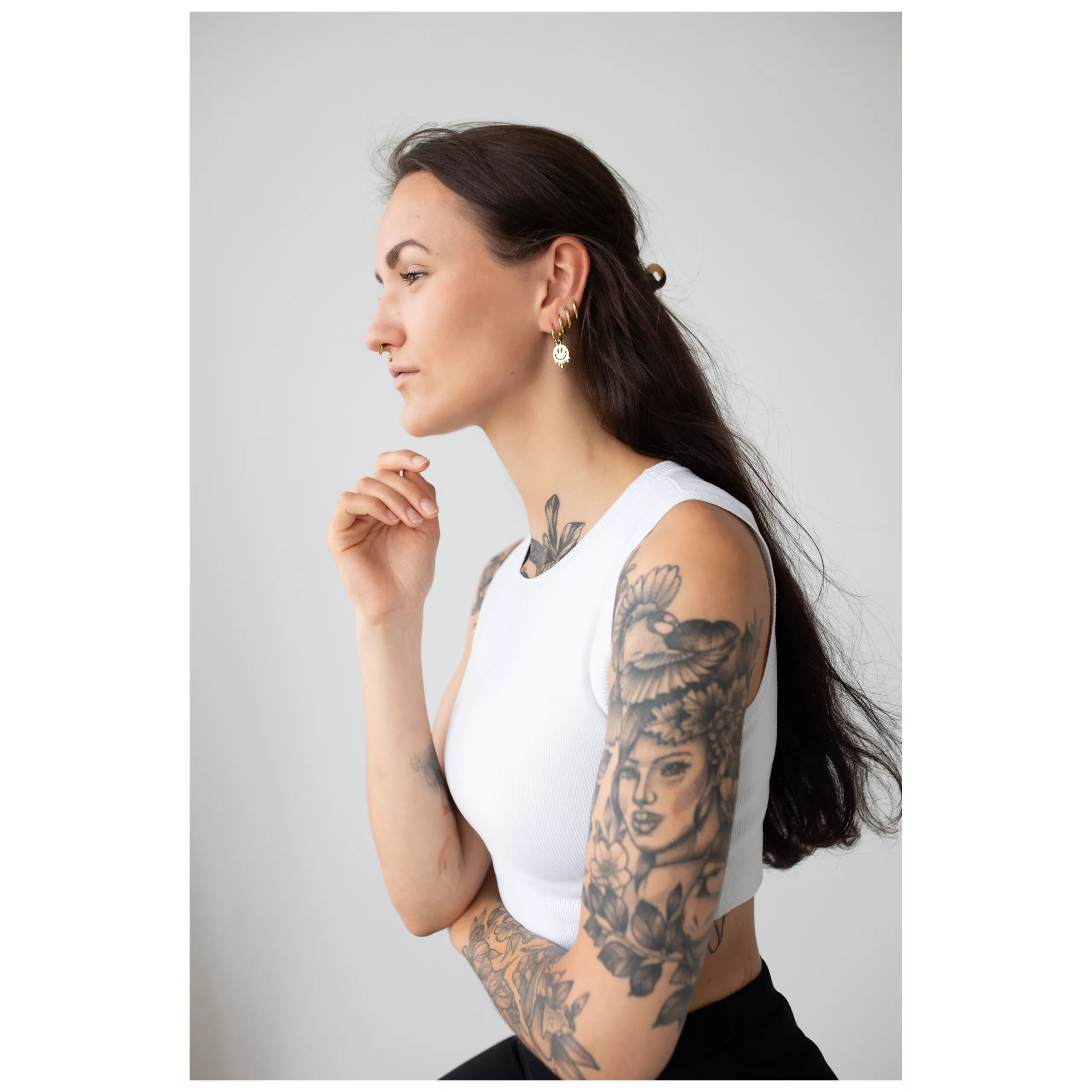 Kultaiset kiiltävät Smiley-korvakorut Pitkähiuksinen nainen käyttää kultaisia Smiley-korvakoruja, neutraali tausta.