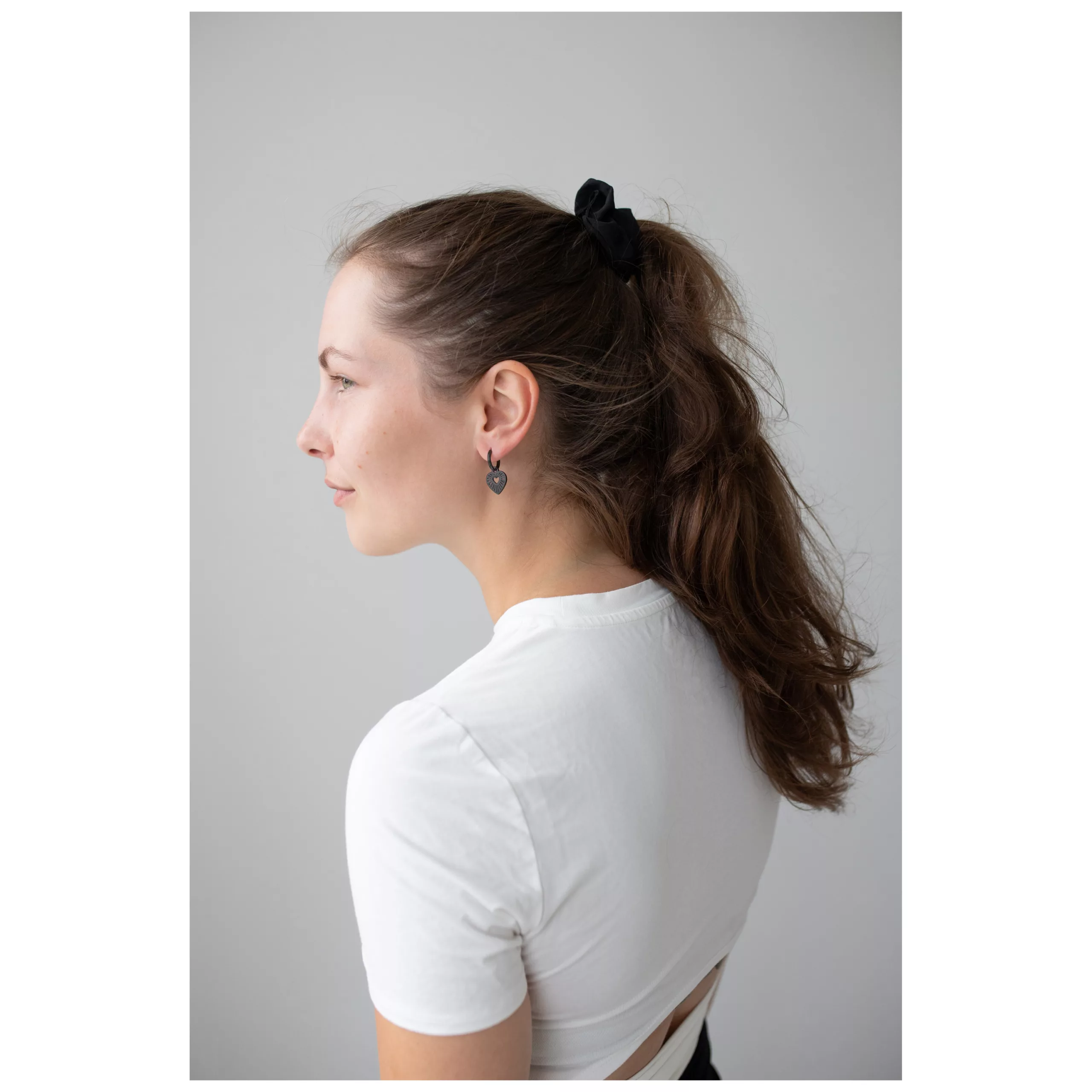 Mustat sydänkorvakorut Wildcatilta Nainen mustilla sydänkorvakoruilla ja valkoisella paidalla harmaata taustaa vasten