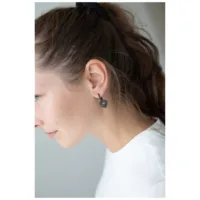 Mustat sydänkorvakorut naiselle Mustat sydämenmuotoiset korvakorut naisen korvissa, jolla on valkoinen paita