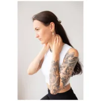 Nainen kultaisilla Little Eye Hoops -korvakoruilla vaaleaa taustaa vasten