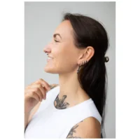 Pitkähiuksinen nainen käyttää pieniä mustia miekka-korvakoruja