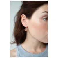 Nainen käyttää ruusukultaisia korvakoruja silmäkuviolla neutraalilla taustalla