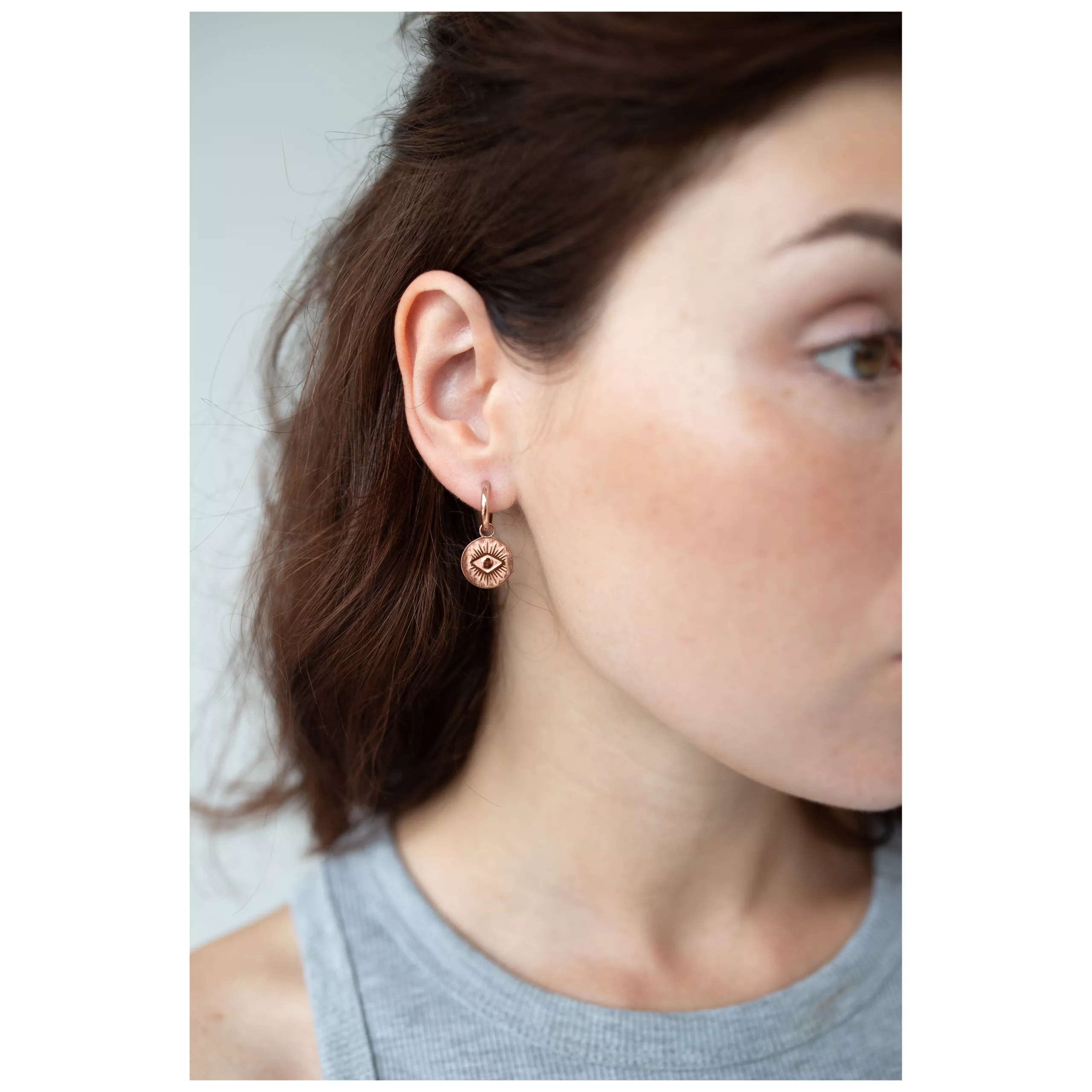 Nainen käyttää ruusukultaisia korvakoruja silmäkuviolla neutraalilla taustalla