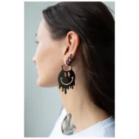 Nainen käyttää suuria mustia Smiley-korvakoruja pisaramotiivilla