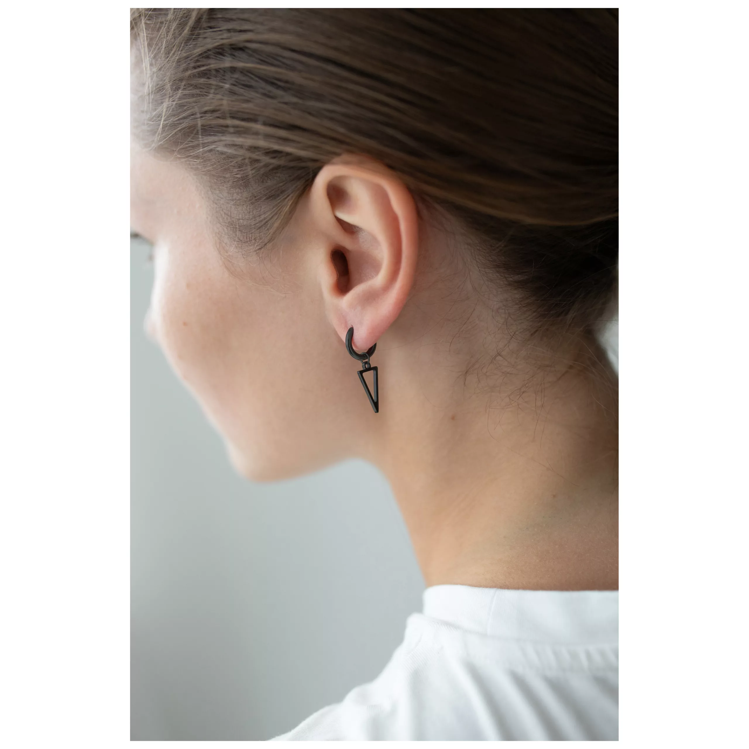 Mustat kolmio-korvarenkaat modernissa tyylissä Nainen mustilla kolmio-korvarenkailla kirurginteräksestä, sivuprofiili