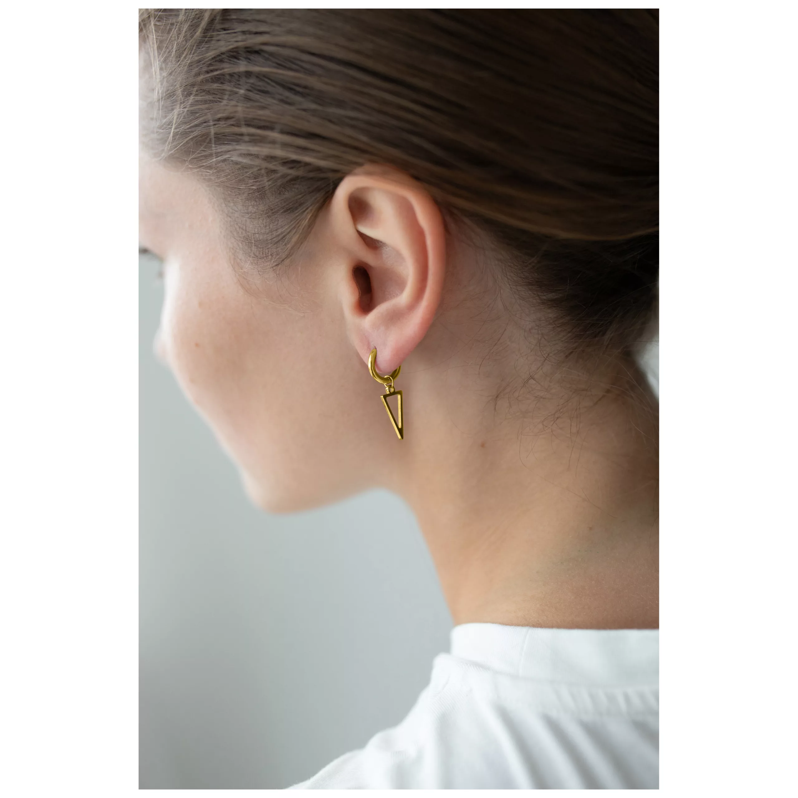 Kultaiset kolmionmuotoiset korvakorut korvassa, sivulta katsottuna