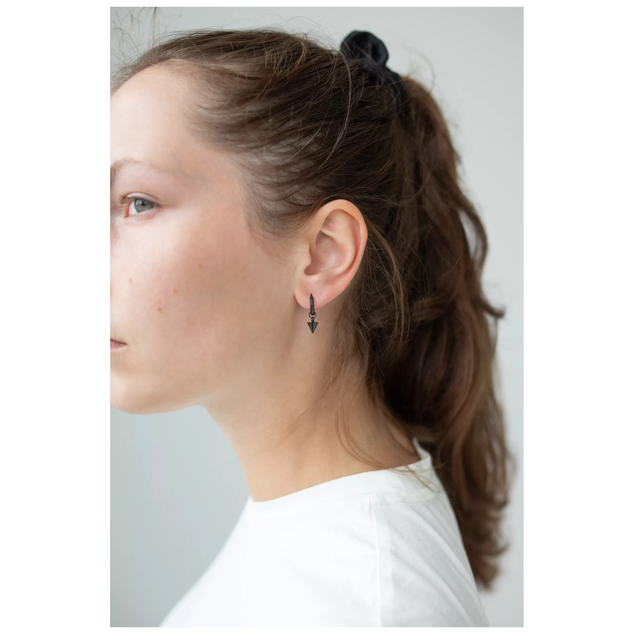 Musta Little Short Spike Hoops -korvakorut Nainen käyttää mustia Hoops-korvakoruja piikillä vaalealla taustalla