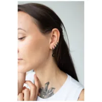 Nainen käyttää mustia Little Moonchild Hoops -korvakoruja neutraalia taustaa vasten