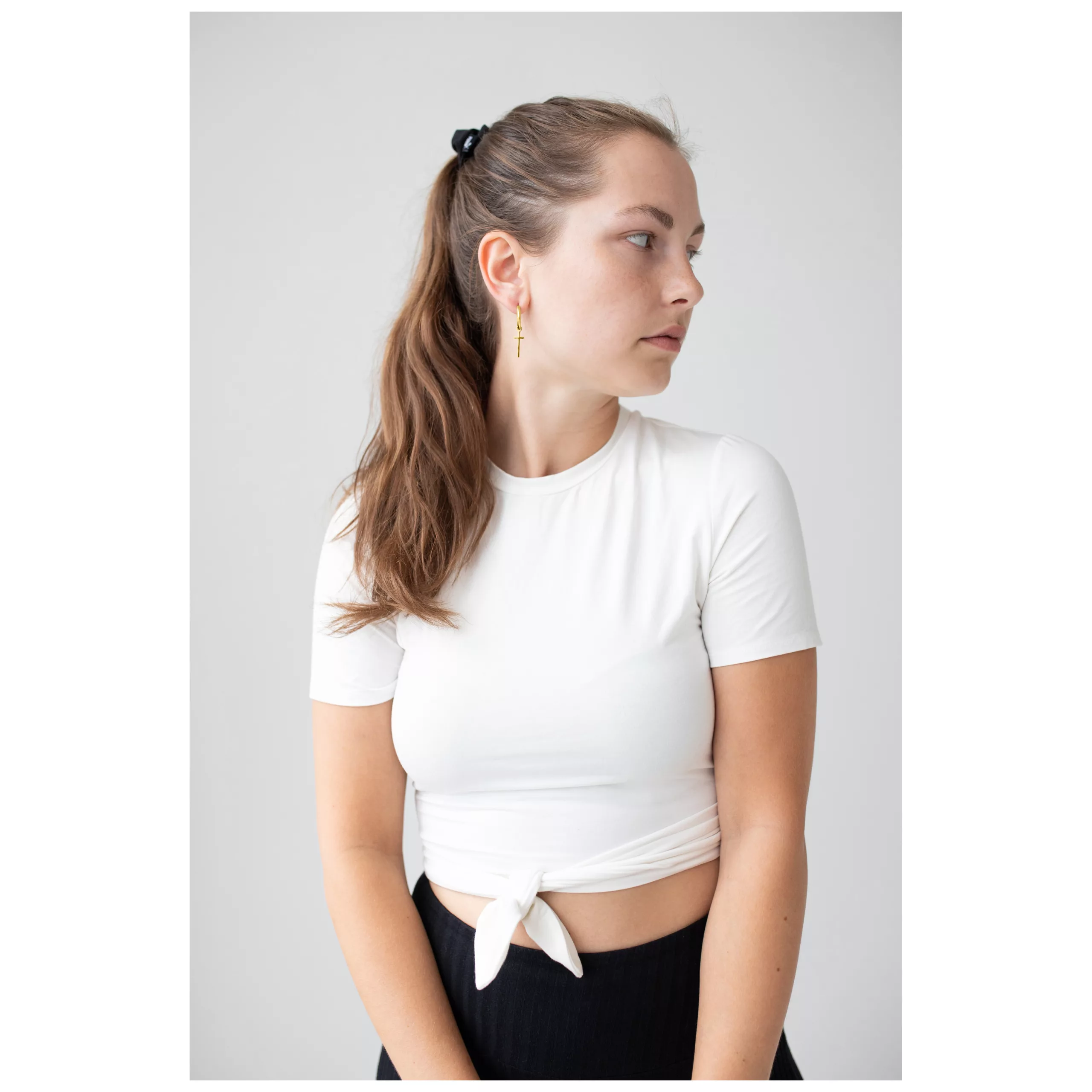 Pitkähiuksinen nainen käyttää kultaisia Little Cross Hoops -korvakoruja