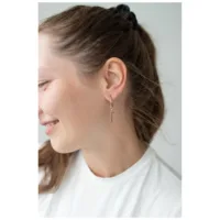 Rosékultaiset renkaat ristiriipuksella naisen korvassa, valkoinen tausta