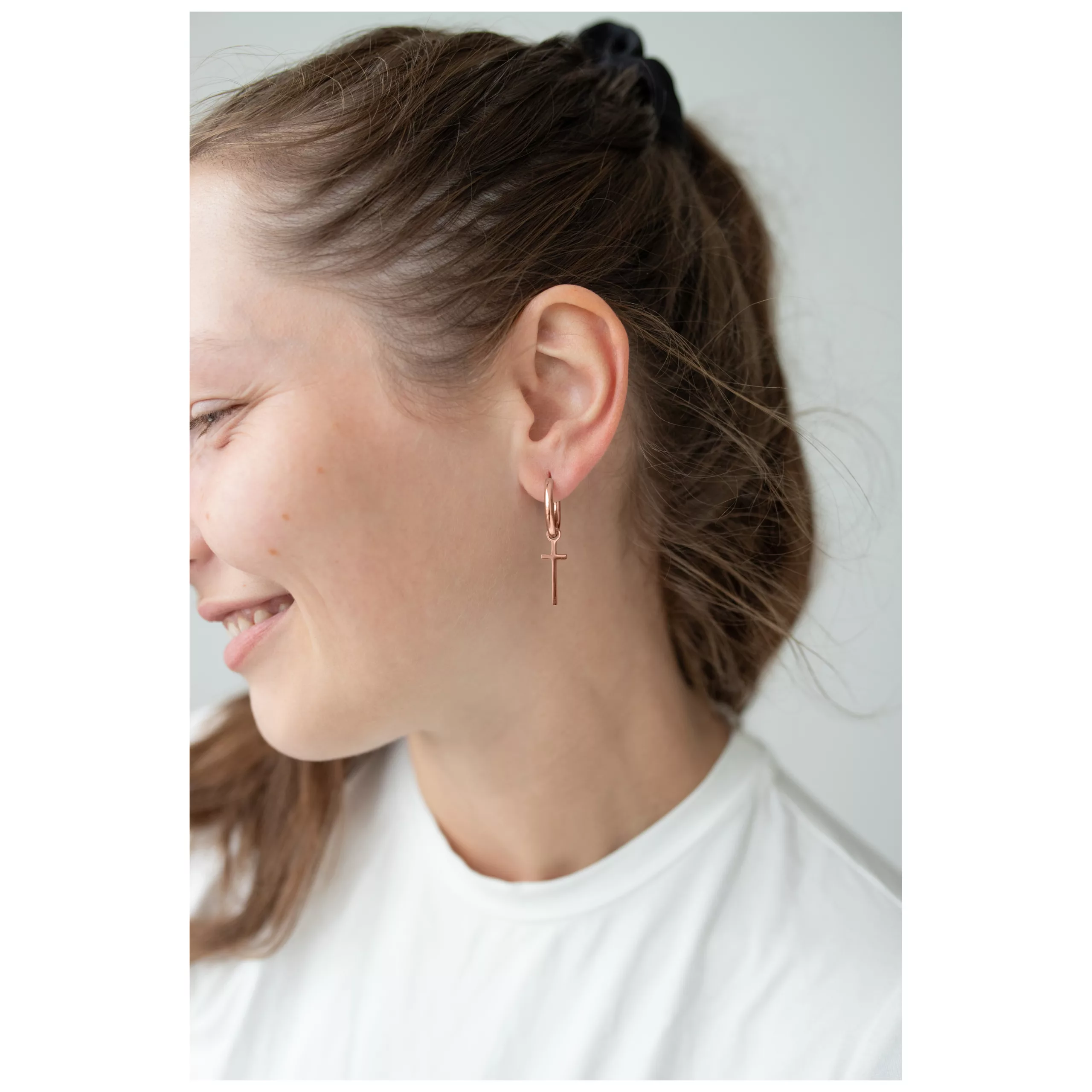 Rosékultaiset renkaat ristiriipuksella naisen korvassa, valkoinen tausta