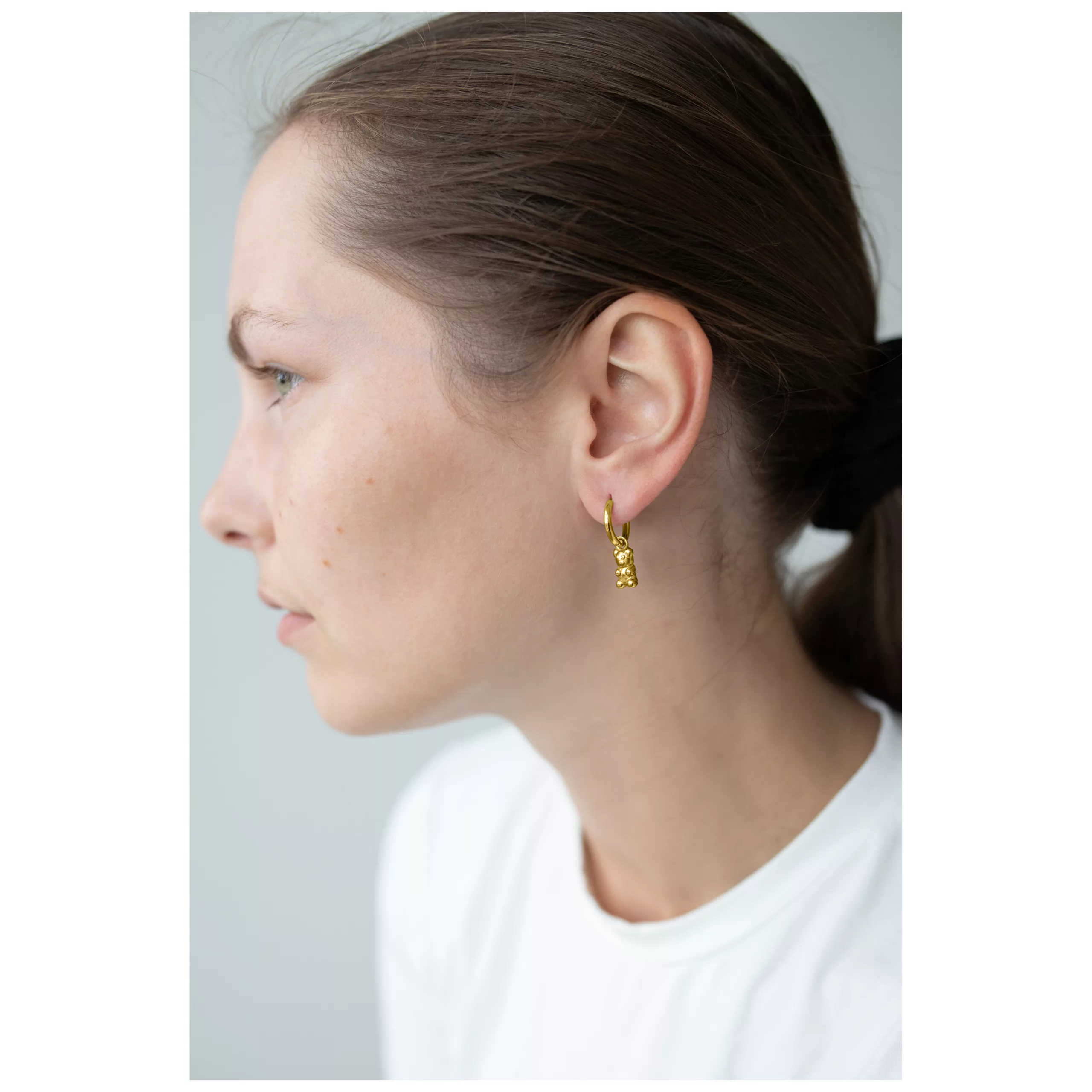 Nainen käyttää kultaisia nallekarkin muotoisia korvakoruja klipsikiinnityksellä