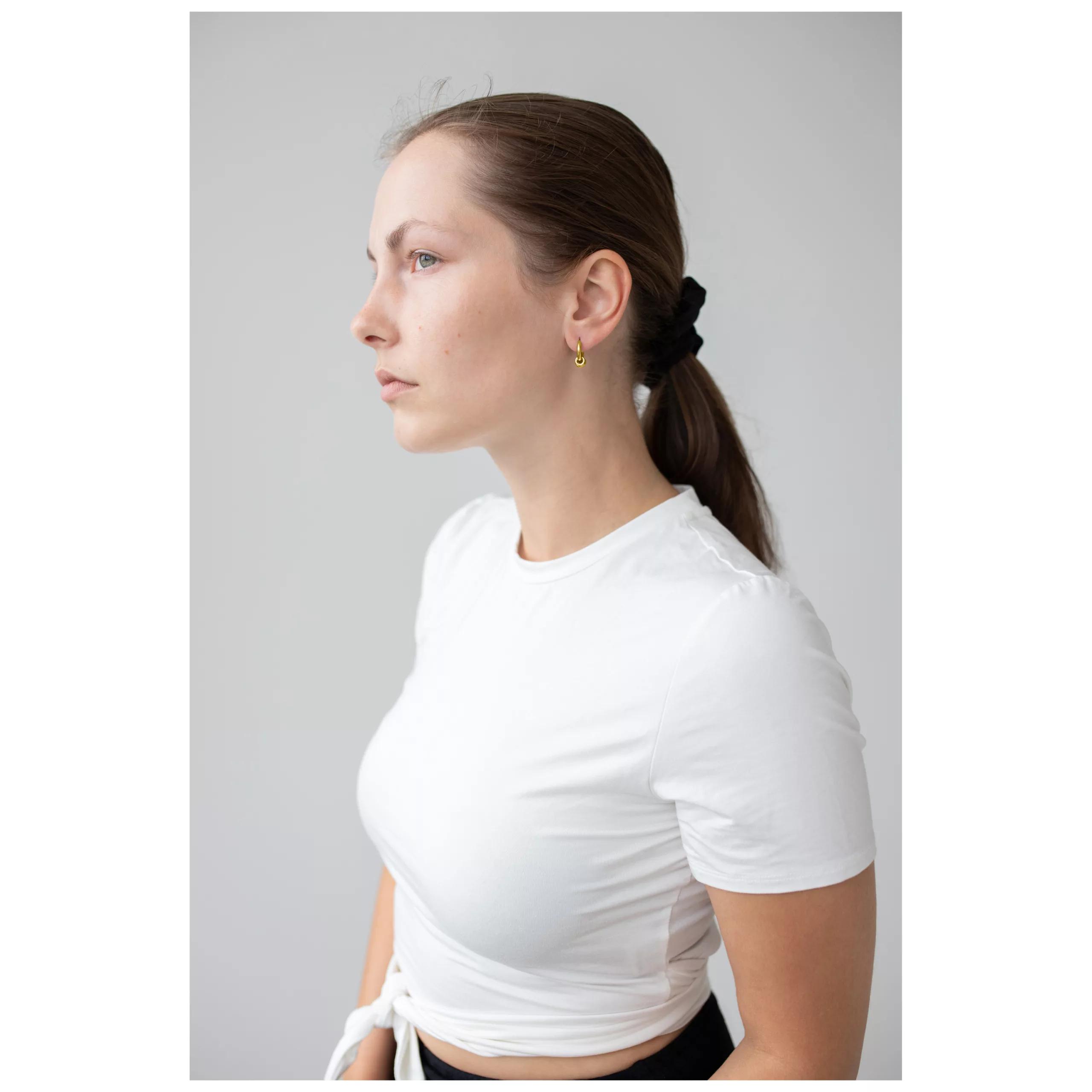 Kultaiset Little 5 Rings Hoops korvassa Nainen kultaisilla Little 5 Rings Hoops korvakoruilla, valkoinen paita, vaalea tausta