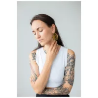 Pitkähiuksinen mustahiuksinen nainen käyttää kultaisia Moon Eclipse Hoops -korvakoruja harmaata taustaa vasten