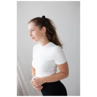 Nainen valkoisessa paidassa käyttää ruusukultaisia korvakoruja neutraalilla taustalla