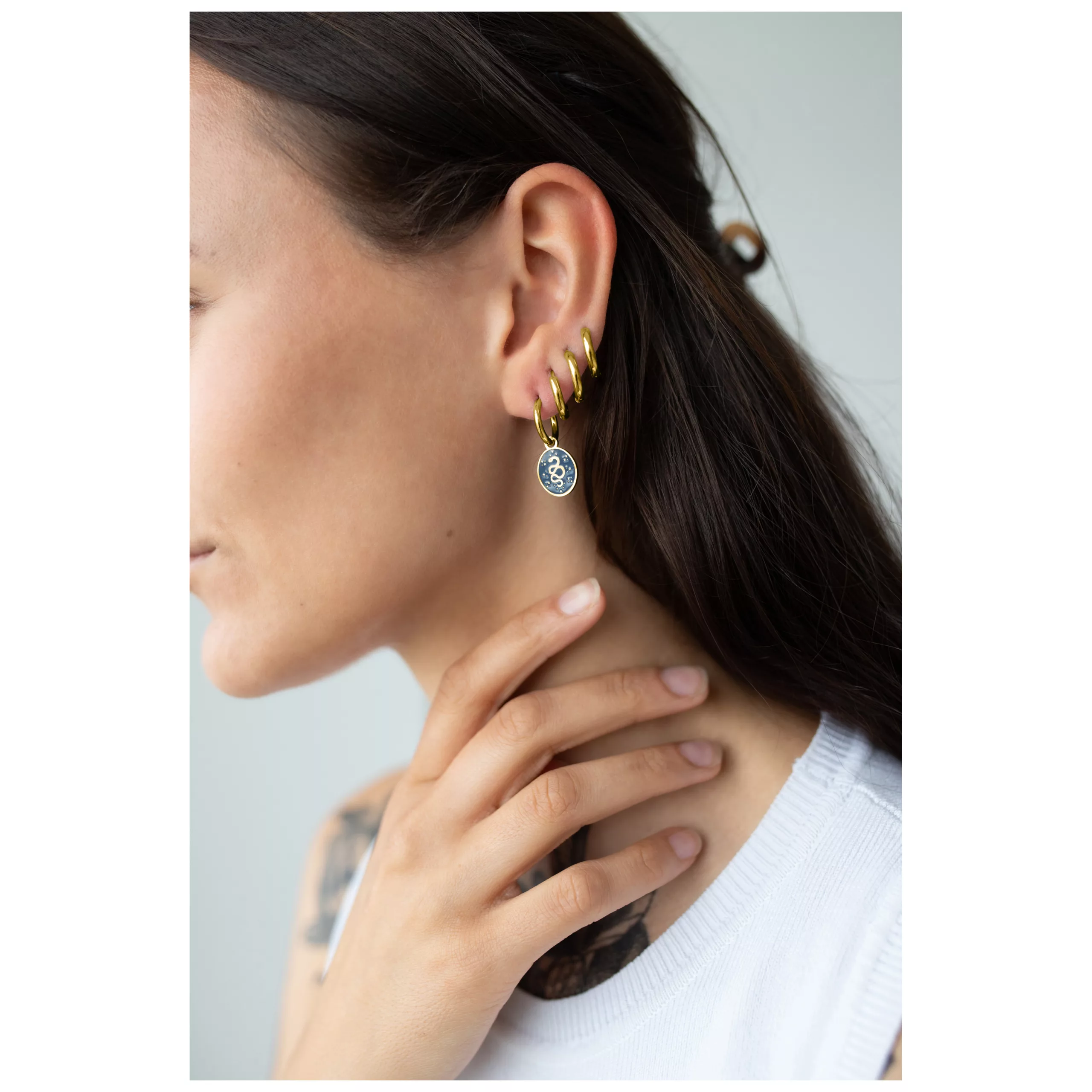 Nainen käyttää kultaisia Little Mystic Snake Hoops -korvakoruja klipsikiinnityksellä