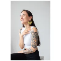 Hymyilevä nainen kultaisilla Selflove Club Hoops -korvakoruilla neutraalilla taustalla