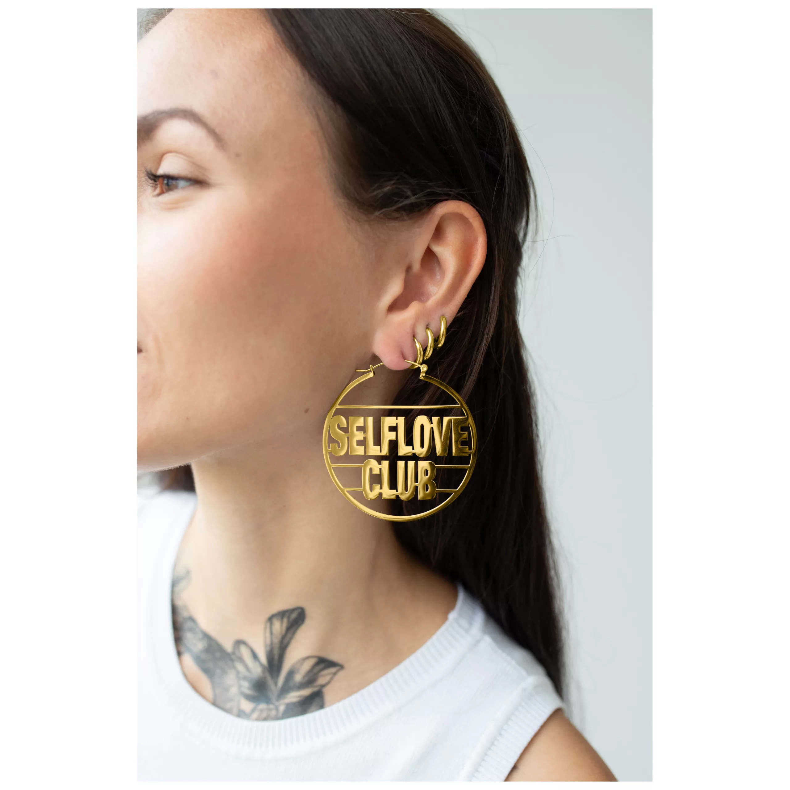 Nainen käyttää suuria kultaisia Hoops-korvakoruja 'Selflove Club' tekstillä