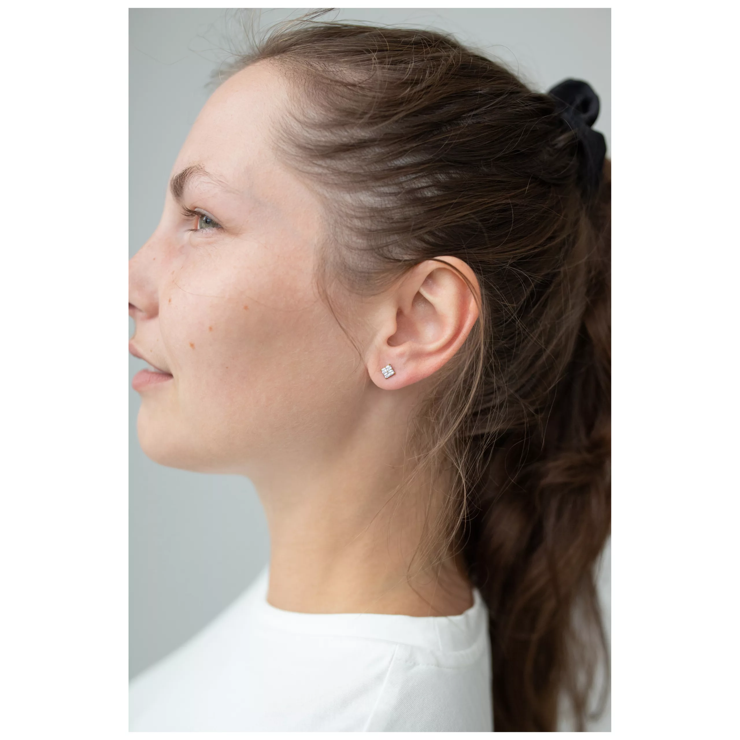 Nainen kultaisilla neliönmuotoisilla kristallikorvakoruilla profiilissa