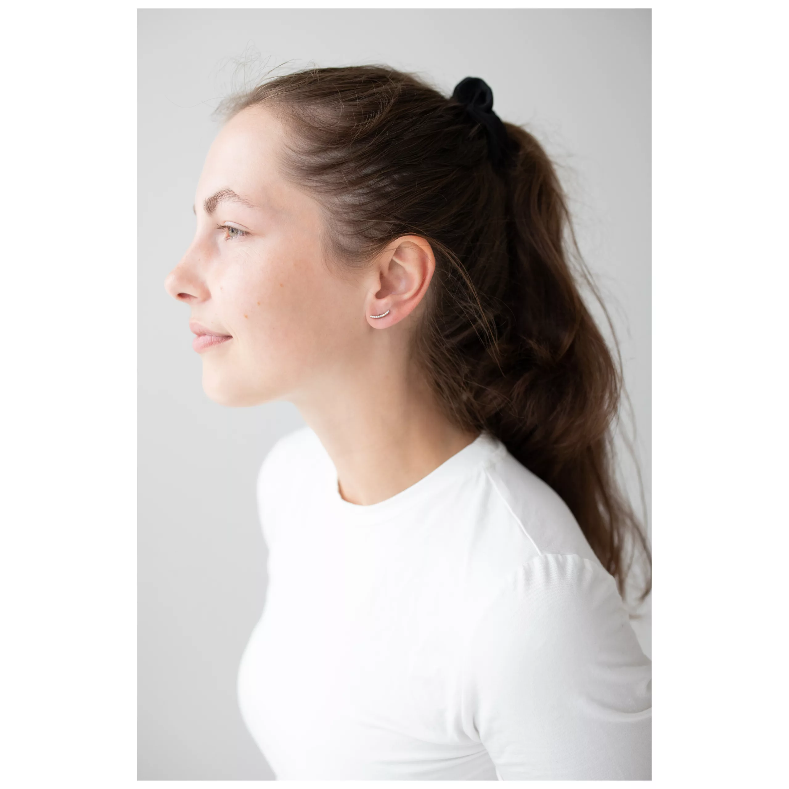 Nainen ruusu-kultaisilla Crystal Arch korvakoruilla, sivuprofiili, valkoinen paita