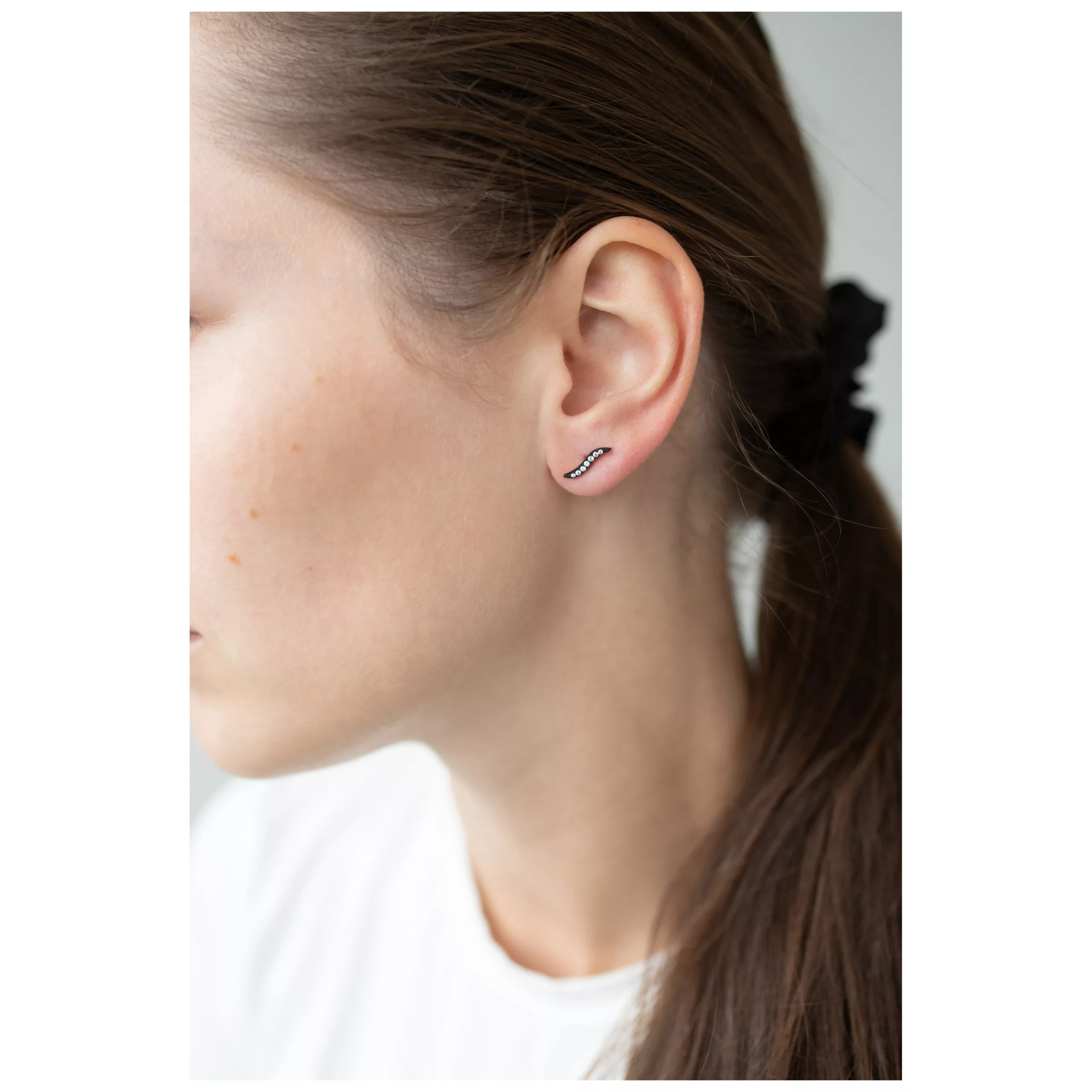 Musta kristalli korvakorut setissä Musta kristalli korvakorut naisen korvassa, jolla on ruskeat hiukset