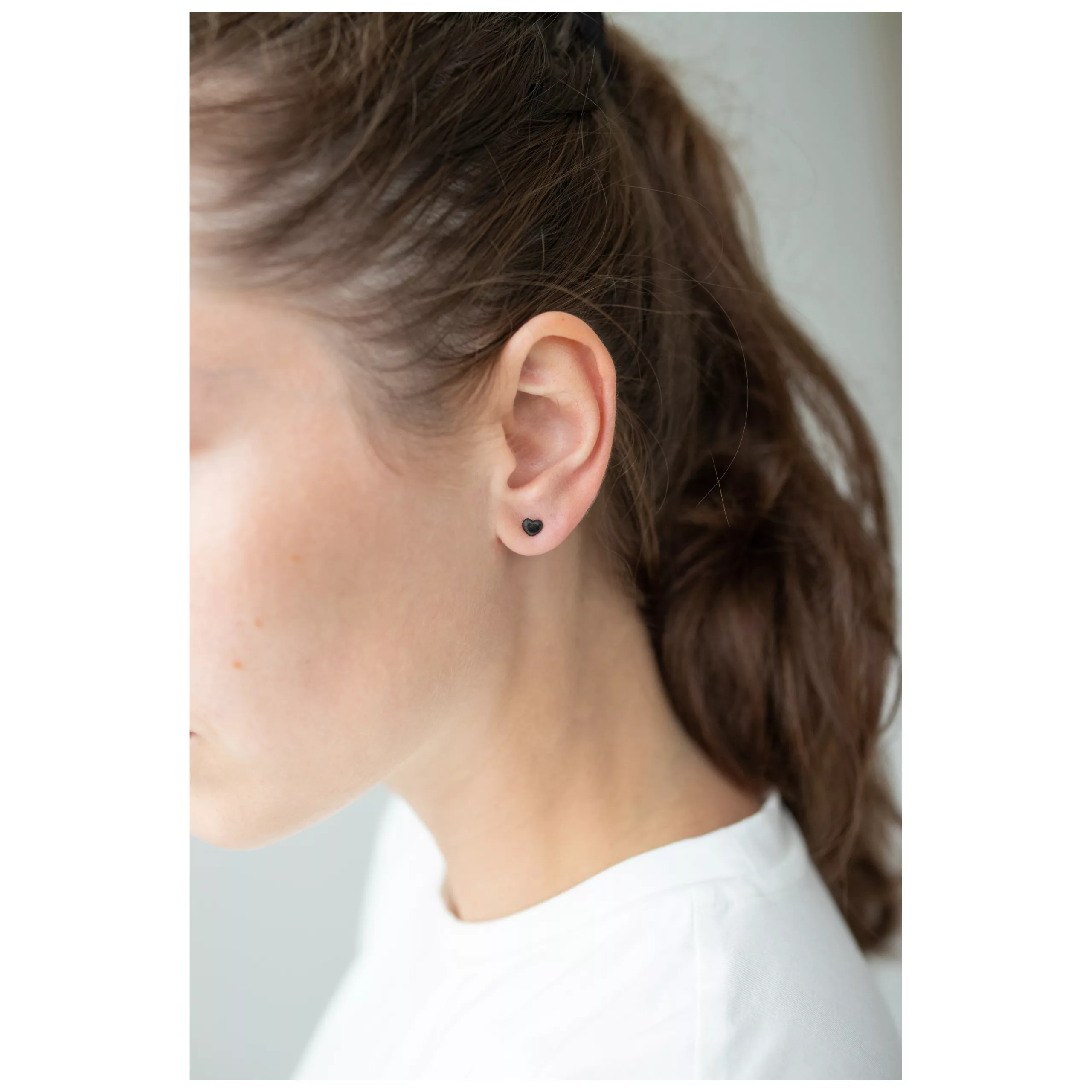 Musta sydän korvakorut naisen korvassa, sivukuva, valkoinen tausta