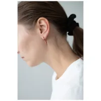 Rosékultaiset Spike-korvakorut Wildcatilta Lähikuva korvasta, jossa on rosékultaiset Spike-korvakorut ja musta hiuslenkki