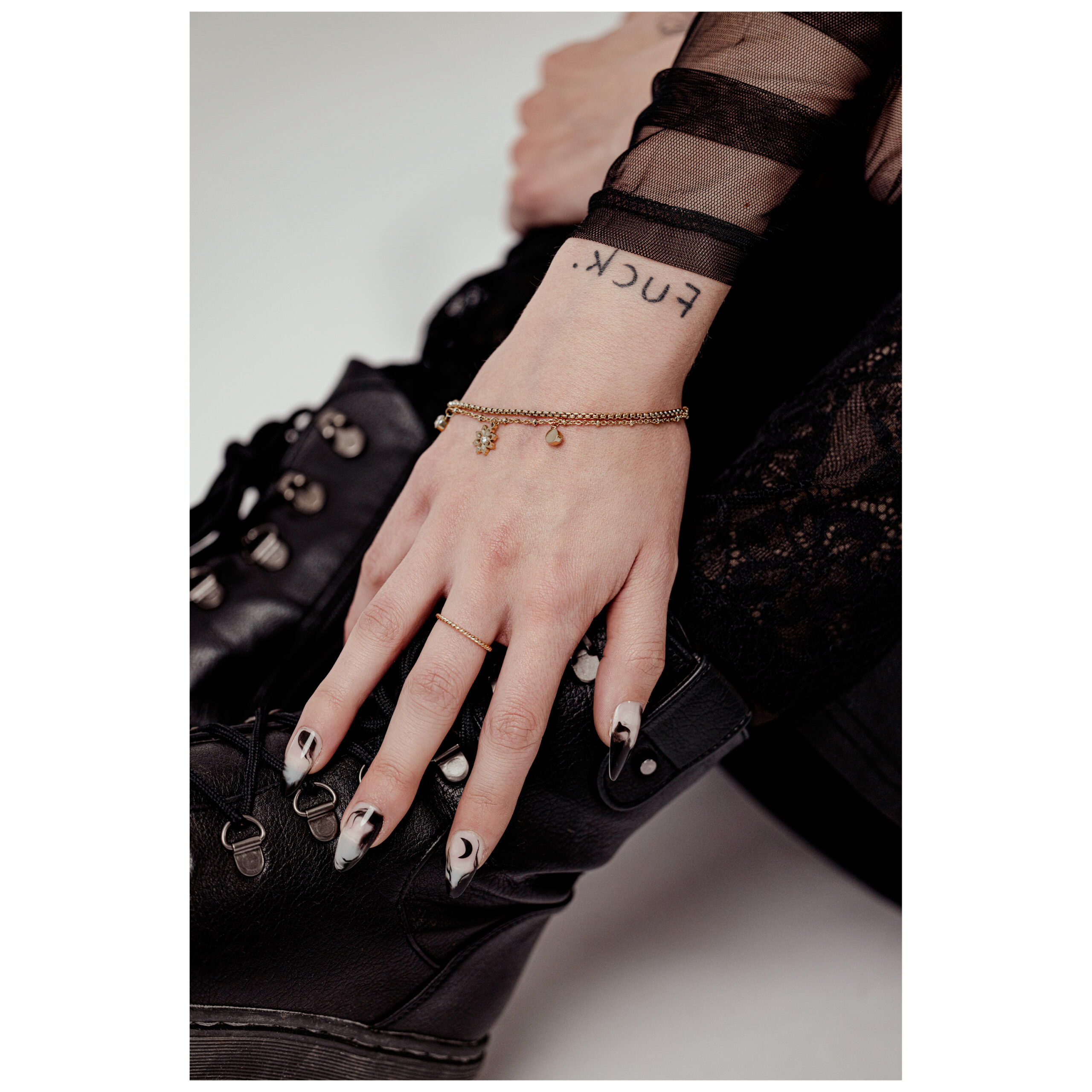 Goldenes Armband mit floralen Elementen auf einer Hand, schwarze Boots im Hintergrund