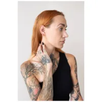 Henkilö, jolla on tatuoitu käsivarsi, käyttää ruusukultaisia Little Bar Hoops -korvakoruja