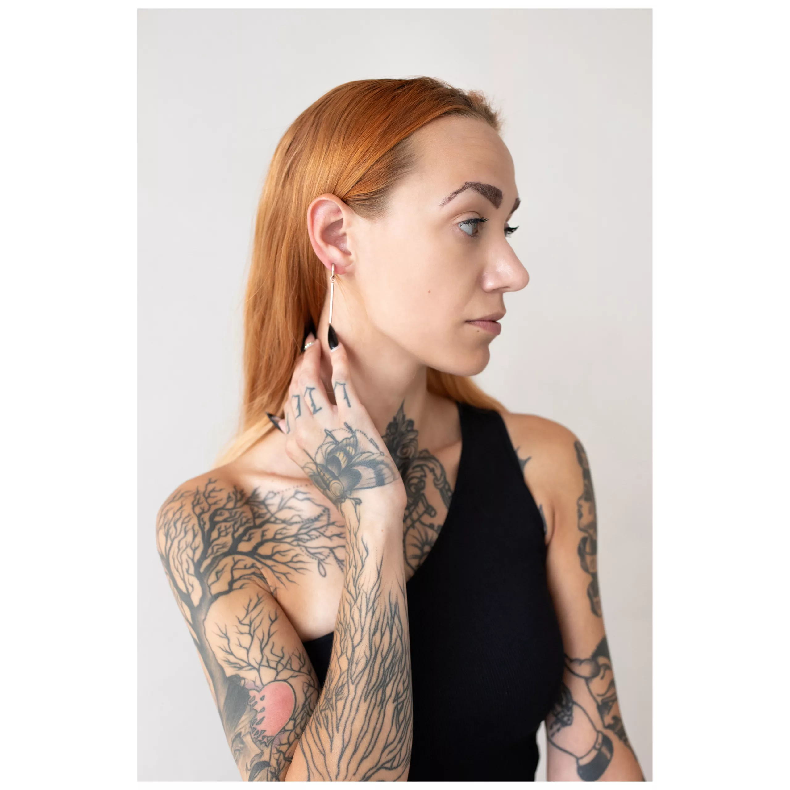 Henkilö, jolla on tatuoitu käsivarsi, käyttää ruusukultaisia Little Bar Hoops -korvakoruja