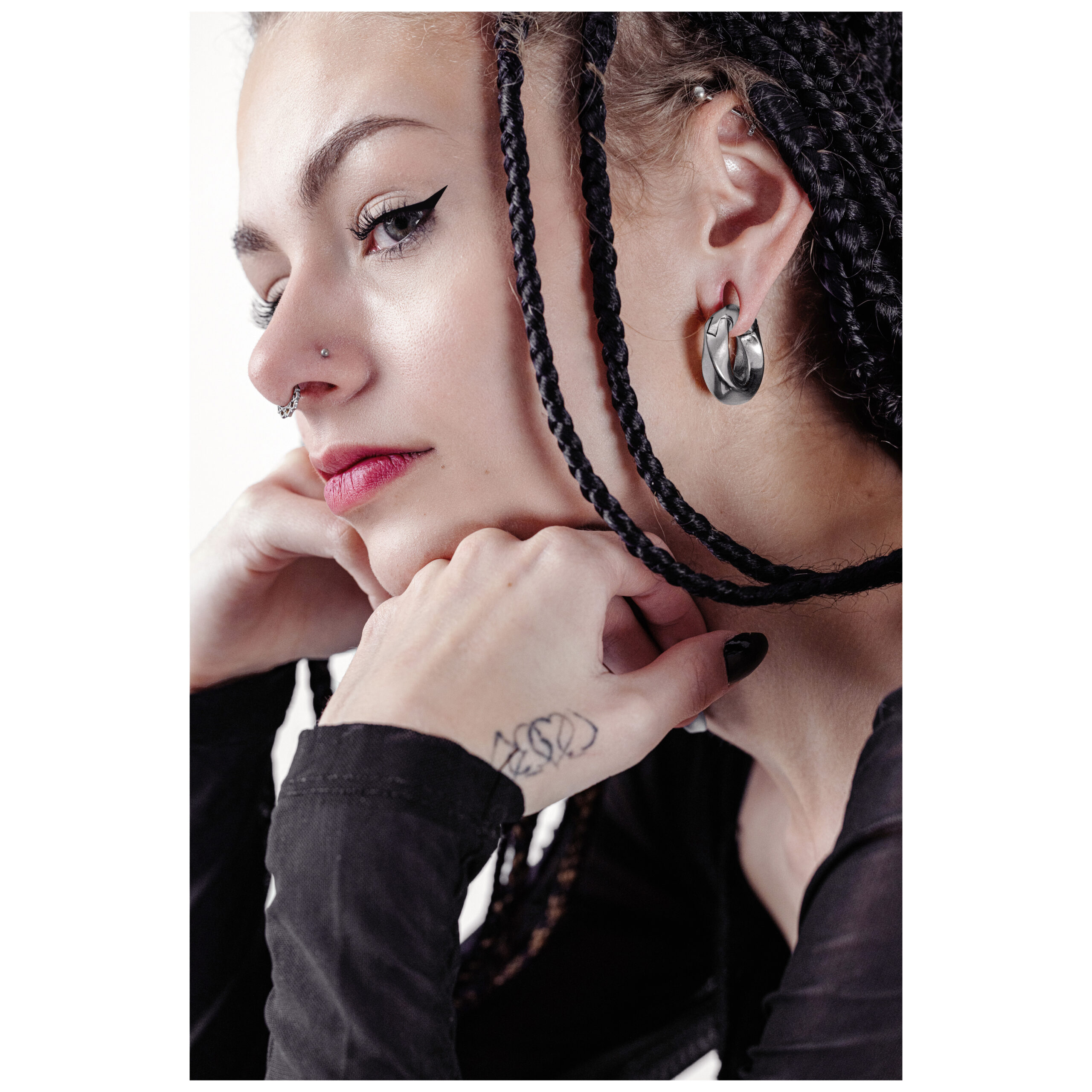 Nainen letitetyillä hiuksilla, jolla on hopeiset Twisted korvapainot ja musta eyeliner