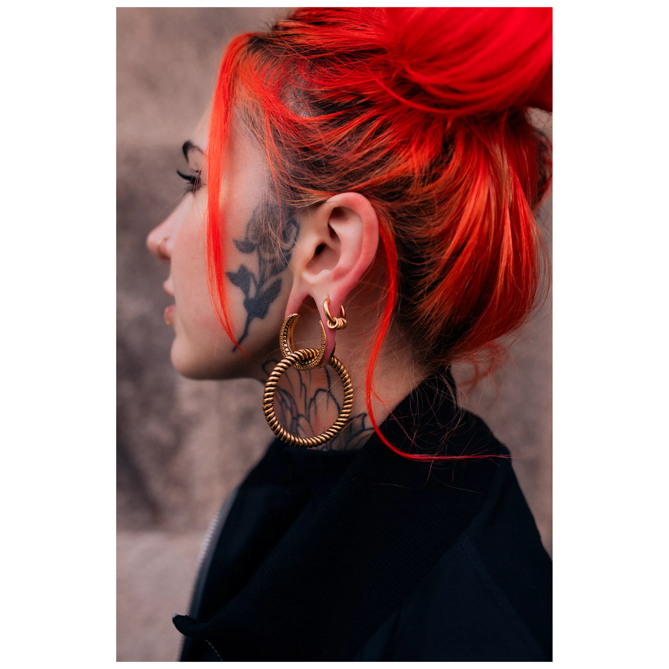 Henkilö, jolla on punaiset hiukset ja kultaiset Twisted Rope korvapainot neutraalilla taustalla