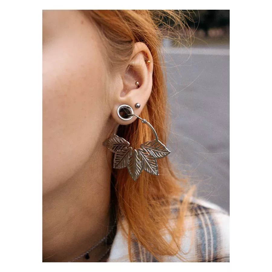 Hopeiset Abey Hoops korvakorut lehtikuviolla naisen korvassa, tausta sumea