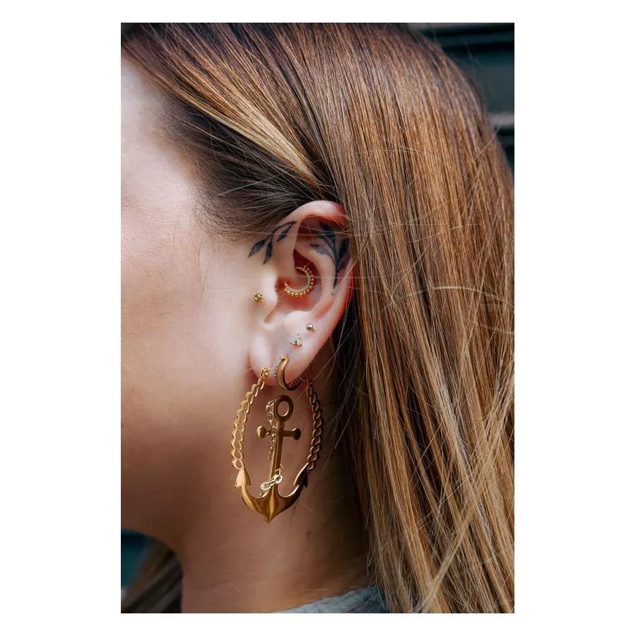 Goldene Ohrringe in Ankerform am Ohr einer Frau mit langem Haar
