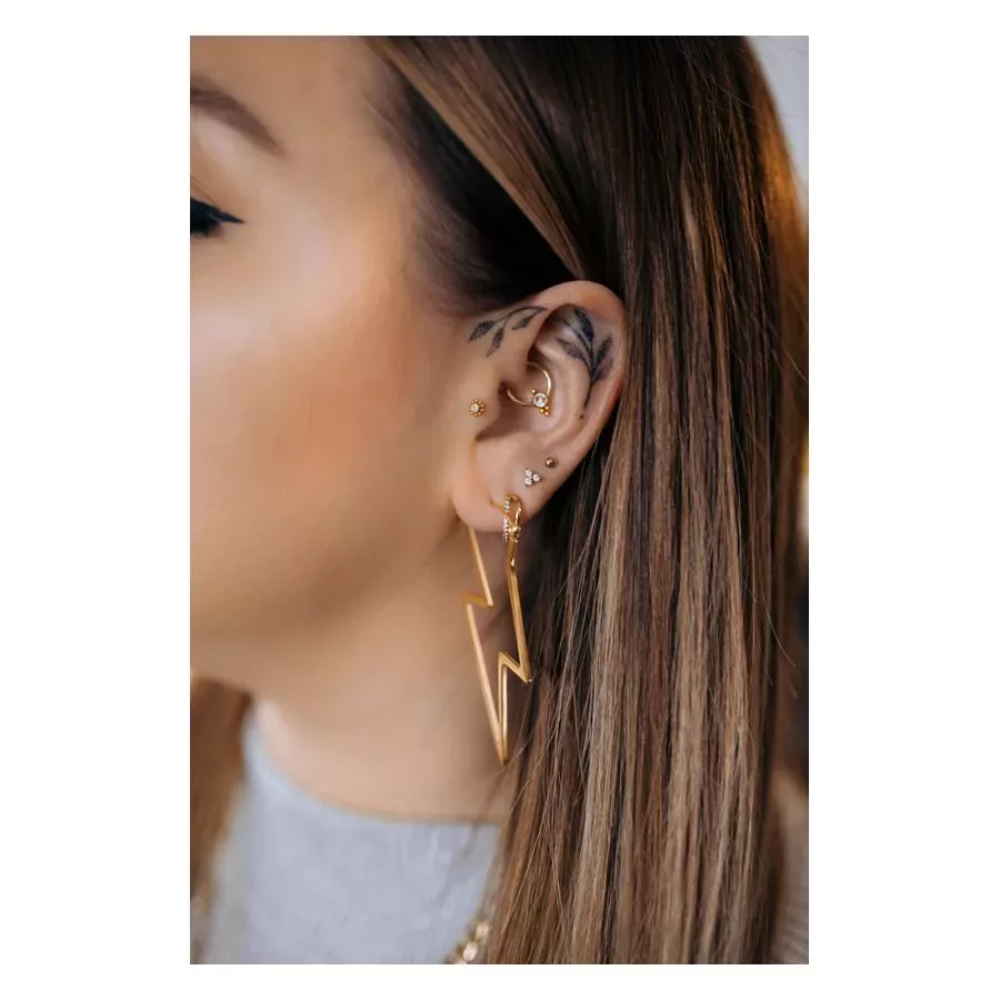 Nahaufnahme eines Ohres mit goldenen Blitz-Ohrringen und mehreren Piercings, neutraler Hintergrund