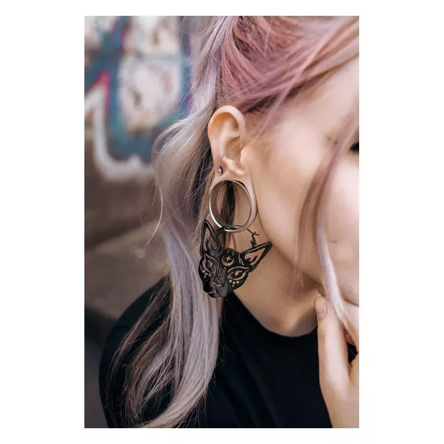 Frau mit Sphynx Hoops in Schwarz, getragen im Ohr, vor urbanem Hintergrund