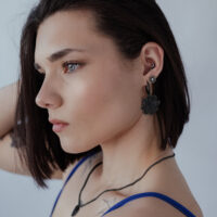 Schwarze Blumen Ohrstecker aus Chirurgenstahl Frau mit schwarzen Blumen Ohrsteckern aus Chirurgenstahl vor neutralem Hintergrund