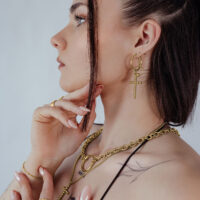 Goldene Bubble Cross Hoops Ohrringe Frau mit goldenen Bubble Cross Hoops Ohrringen vor hellem Hintergrund