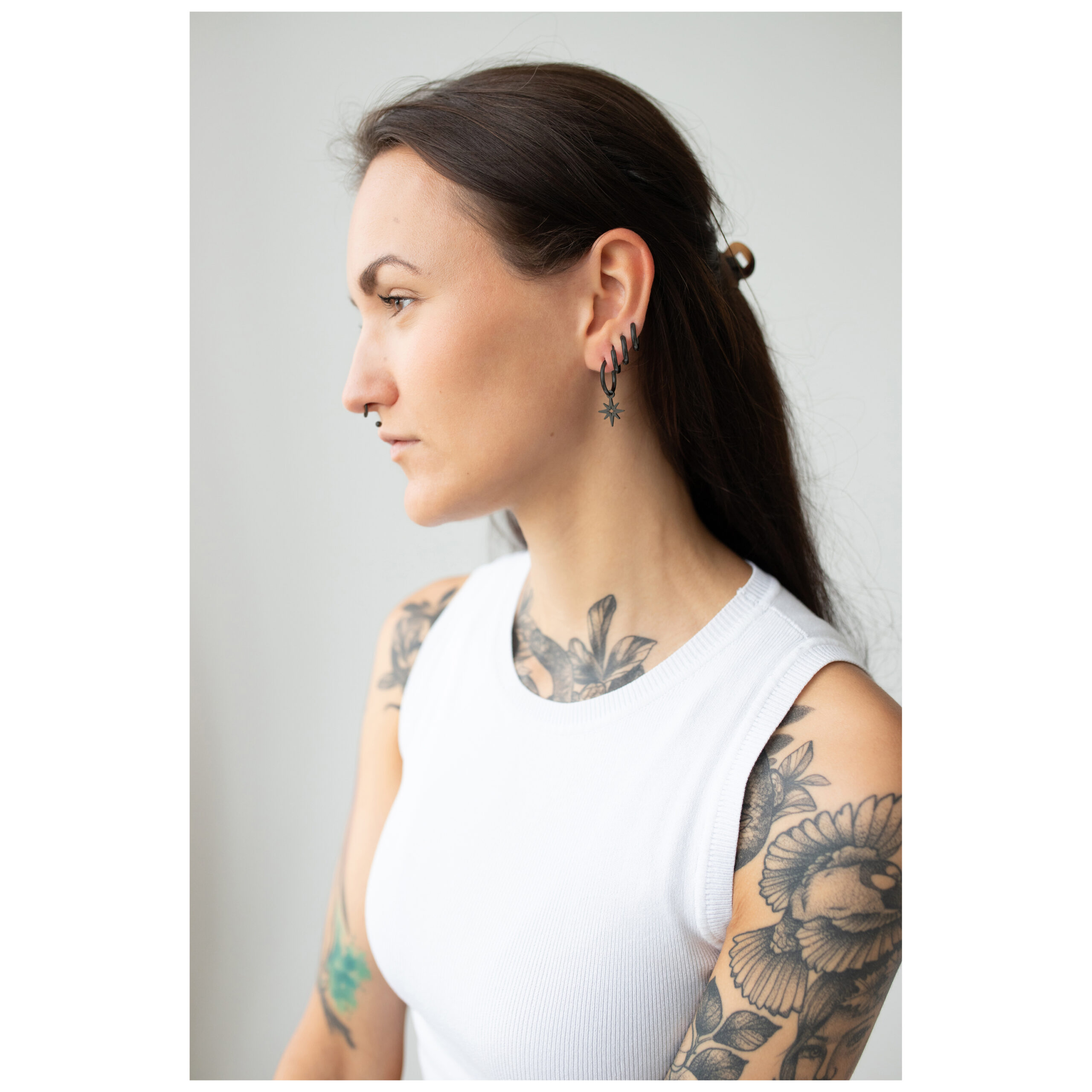 Musta Little Polar Star Hoops -korvakorut Nainen, jolla on mustat Little Polar Star Hoops -korvakorut korvassa, tatuoinnit näkyvissä