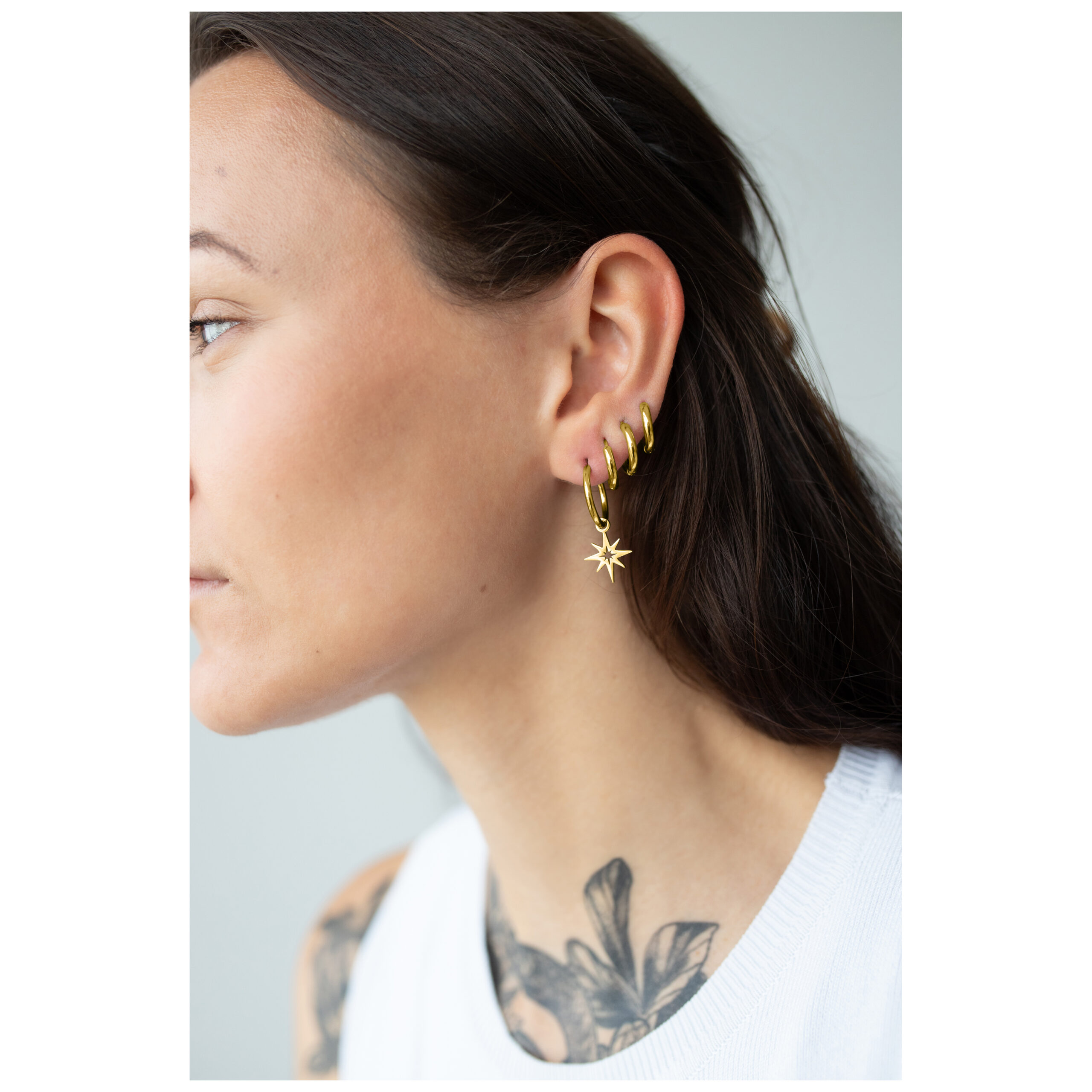 Nainen, jolla on Little Polar Star Hoops kultaisesta metallista korvassa, sivulta kuvattuna