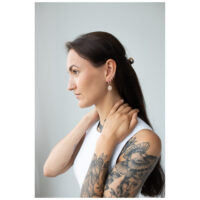 Pitkähiuksinen nainen käyttää ruusukultaisia mandala-korvakoruja, sivuprofiili vaalealla taustalla