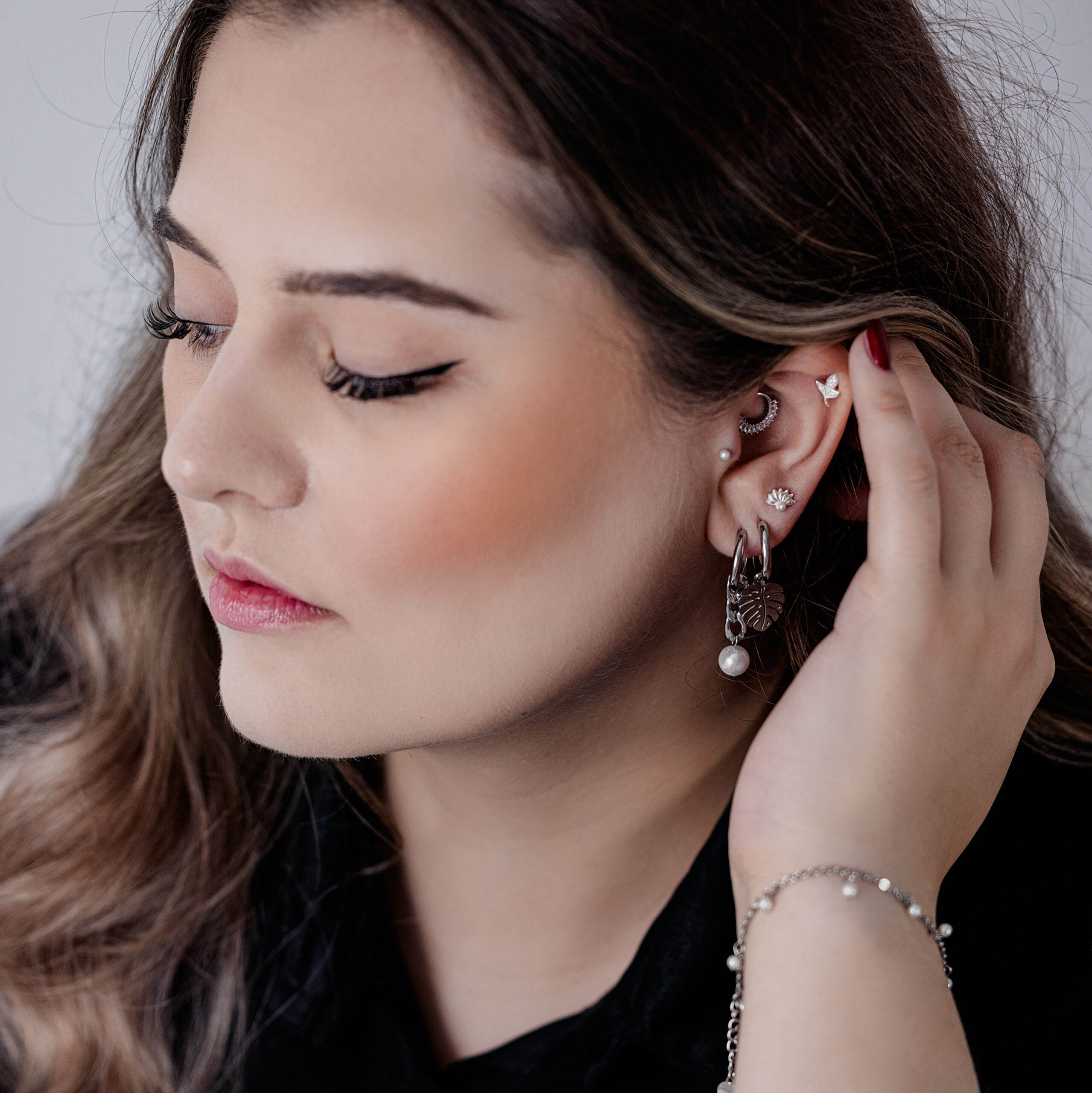 Nahaufnahme einer Frau mit silbernen Monstera Leaf Ohrringen und mehreren Piercings