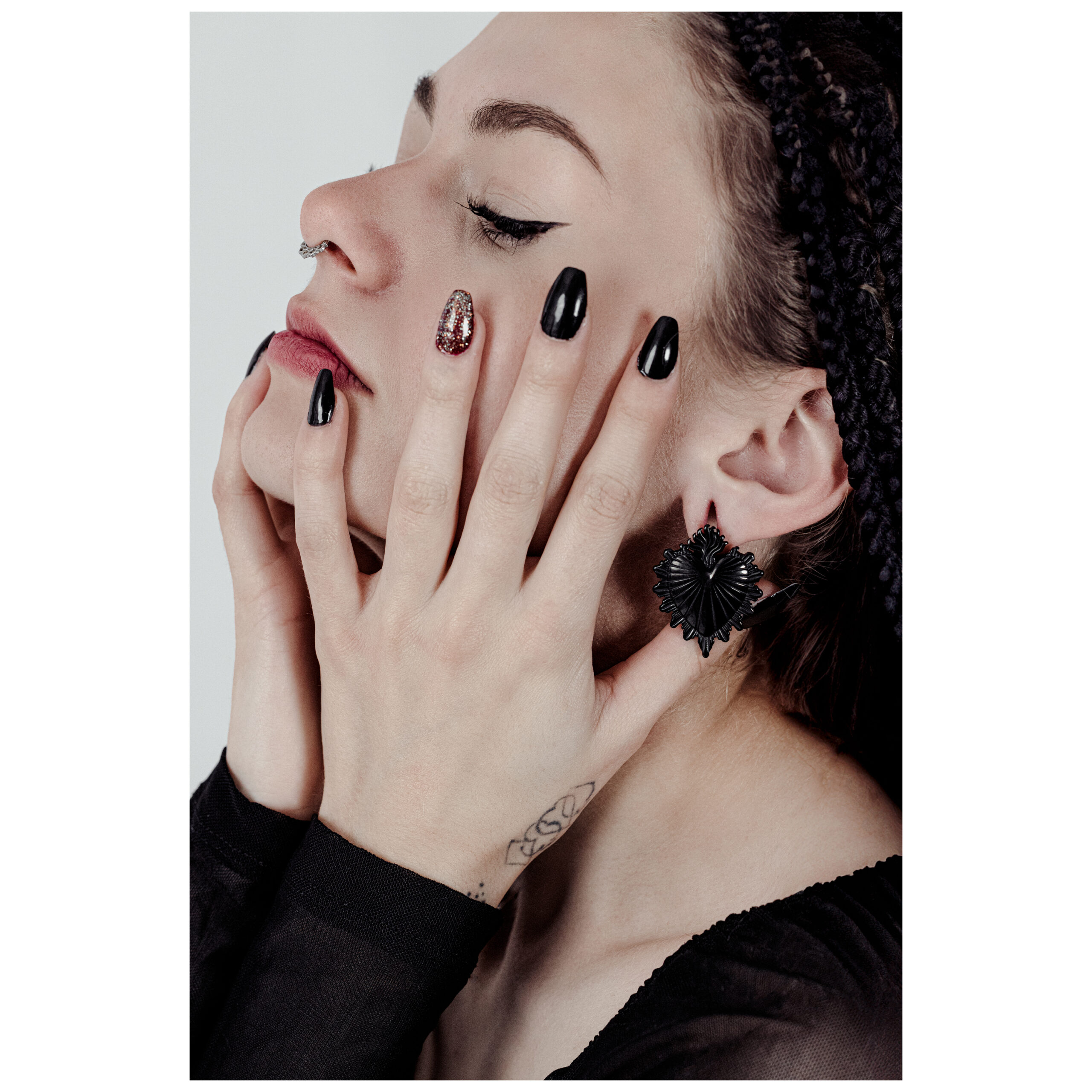 Frau mit goldenen Sacred Heart Ohrgewichten und schwarzem Top vor neutralem Hintergrund