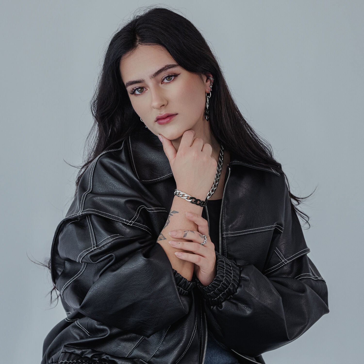 Pitkähiuksinen nainen, jolla on mustat hiukset, käyttää hopeisia Wildcat Hoopseja harmaata taustaa vasten